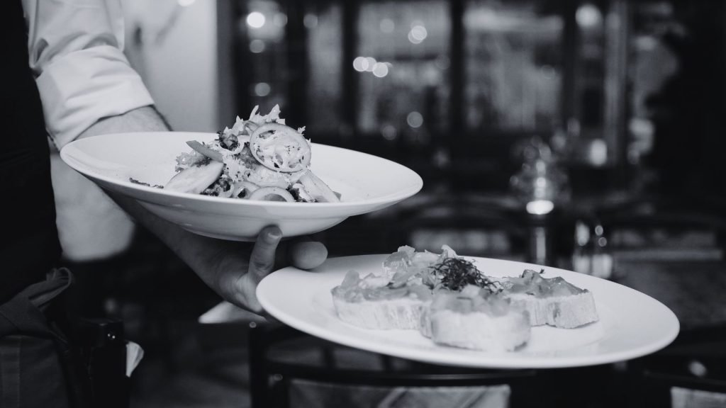 Sales Lessons From Your Next Dinner Out - Black and white photo of a server holding two plates in one hand